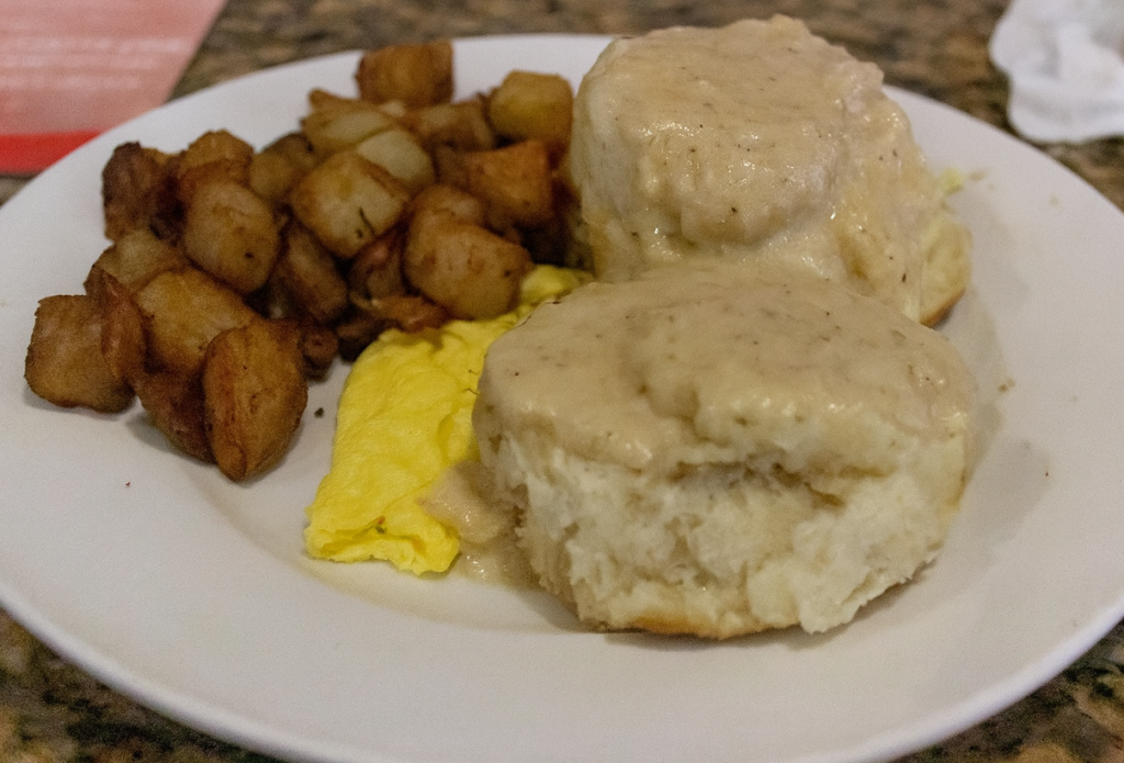 Biscuits and gravy, with potatoes and eggs on a white plate.